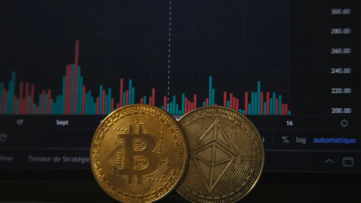 Moedas de bitcoin e ether diante de gráfico de cotação em tela