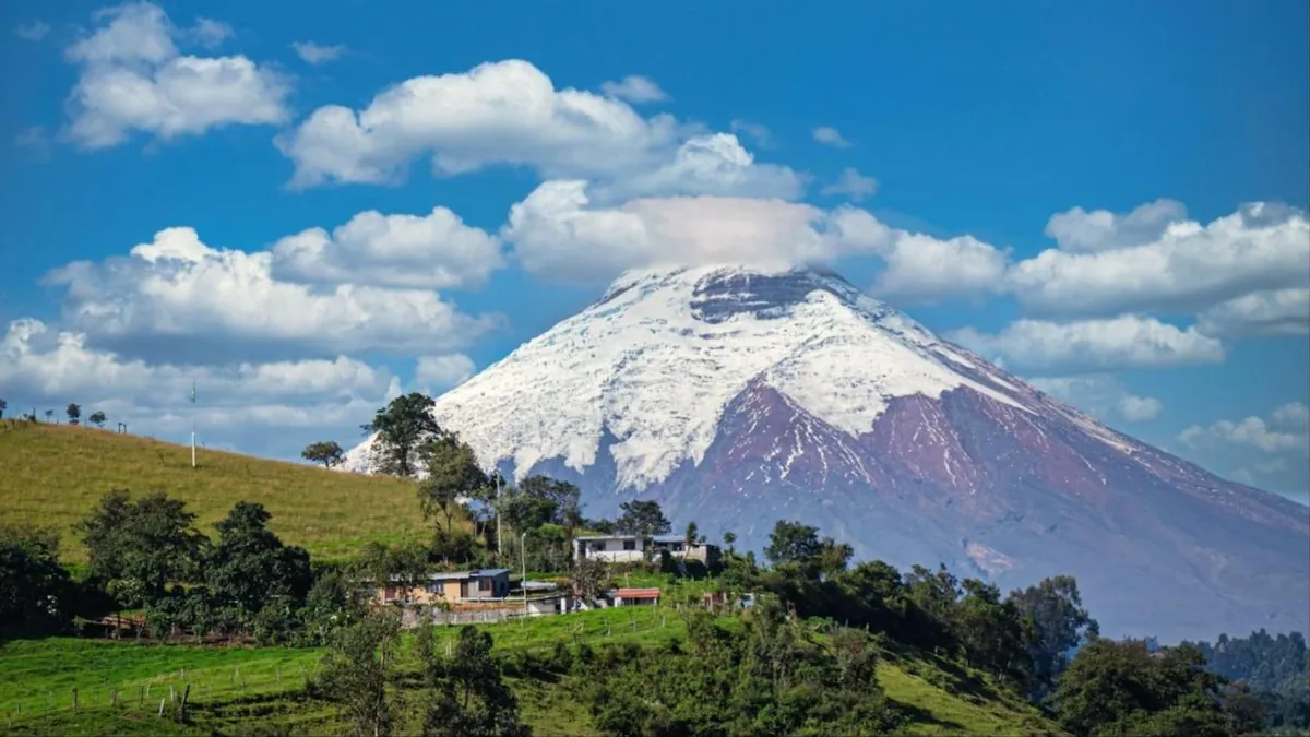 Vulcão nevado nos Andes do Equador, com casas e campos verdes