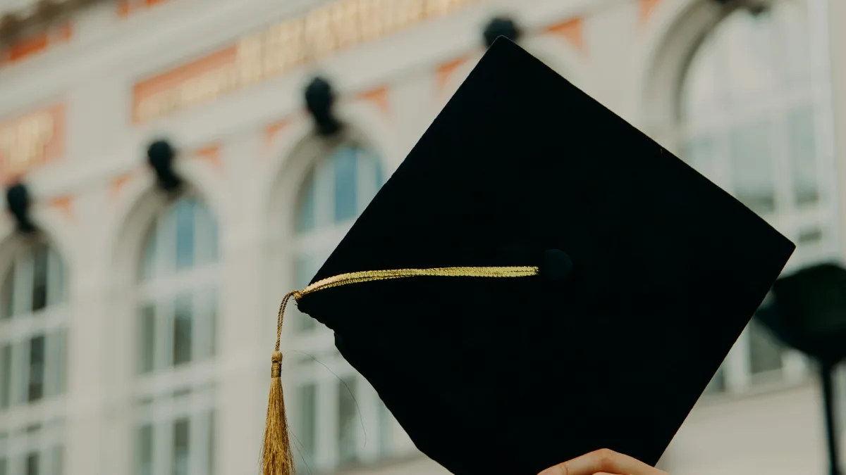 Capelo de formatura preto em primeiro plano, diante de prédio universitário
