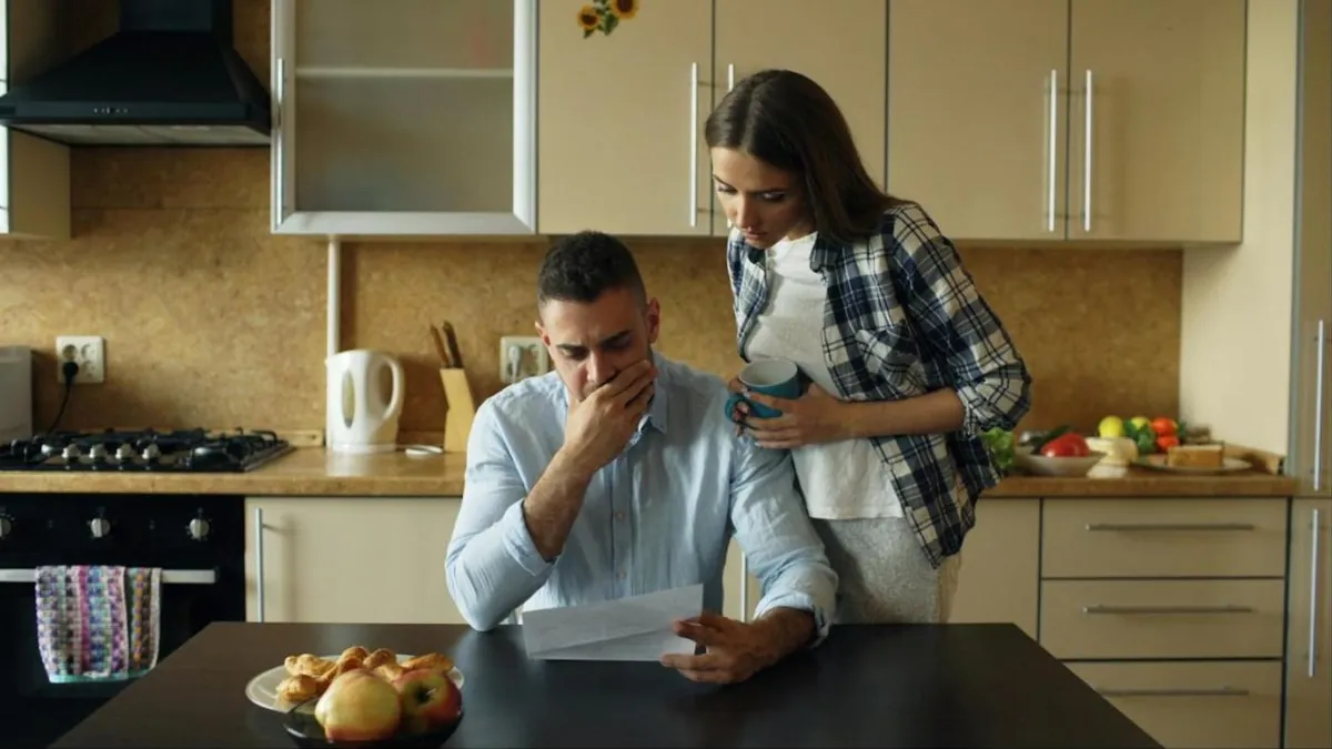 Casal preocupado lê conta na mesa da cozinha, retrato do endividamento das famílias